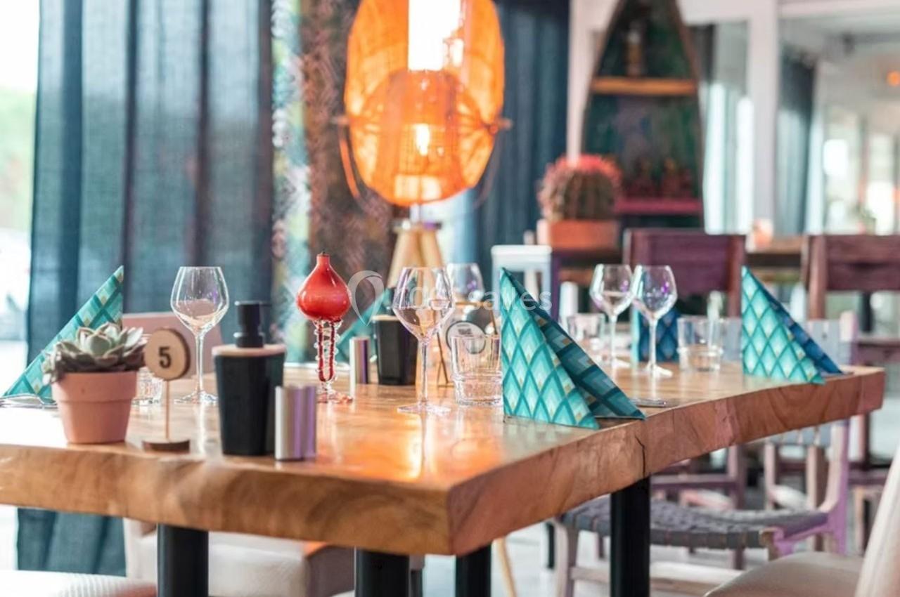 Table dressée avec des verres, serviettes pliées en triangle et décoration dans un restaurant lumineux.