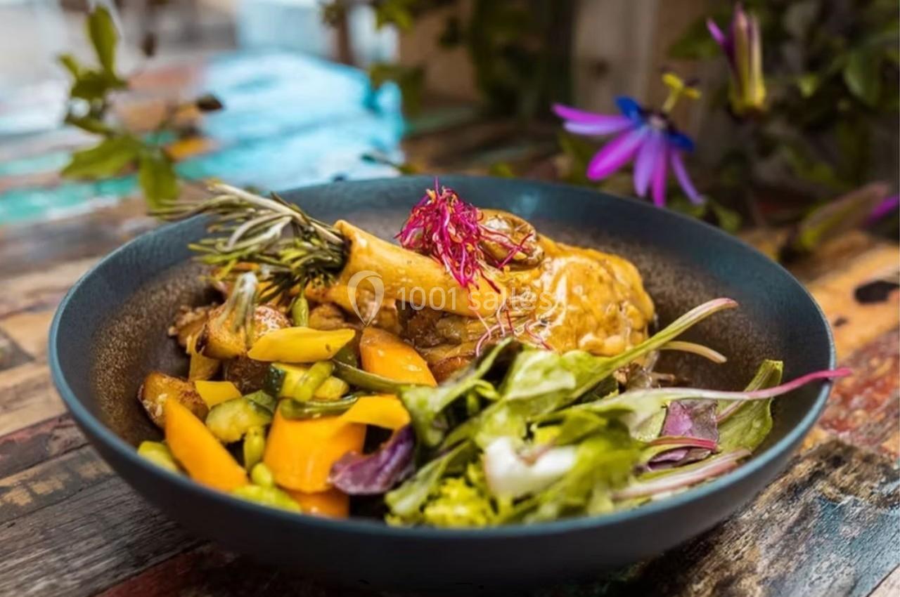 Assiette de légumes colorés avec une garniture de viande, herbes et fleurs comestibles, présentée sur une table en bois.