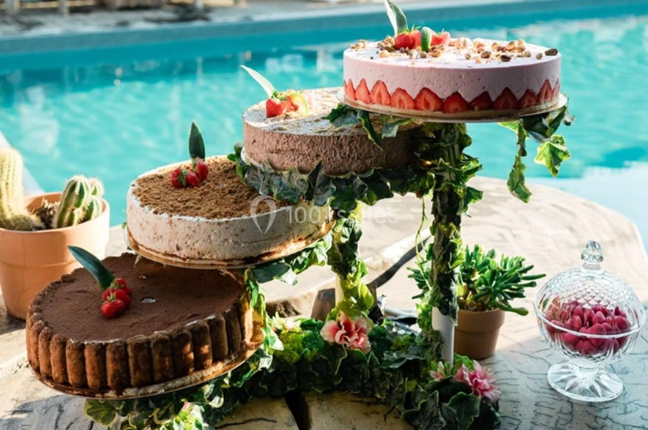 Quatre gâteaux variés présentés sur un présentoir décoré de feuillage, près d'une piscine en extérieur.
