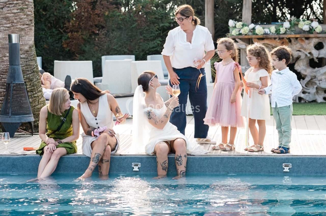Des adultes et des enfants discutent et jouent au bord d'une piscine dans un cadre extérieur ensoleillé.