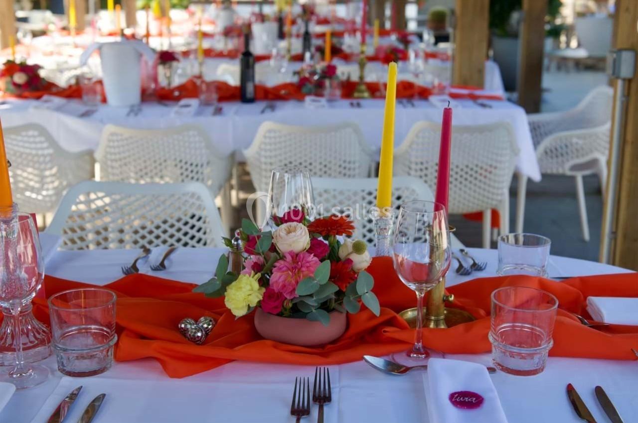 Table dressée avec nappes blanches, chemins de table rouges, bougies colorées et centre de table floral.