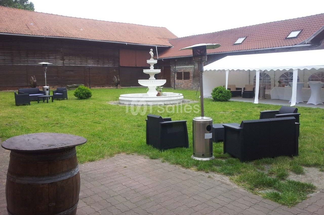 Cour intérieure avec fontaine centrale, mobilier de jardin noir, tonnelle blanche et bâtiments en bois autour.