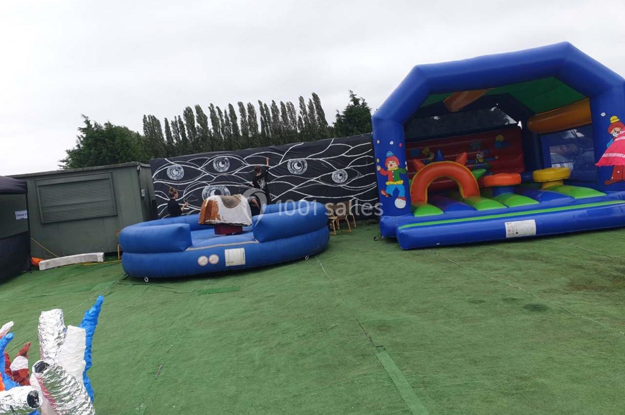 Structures gonflables colorées sur une surface en gazon synthétique, avec des arbres et un mur décoré en arrière-plan.