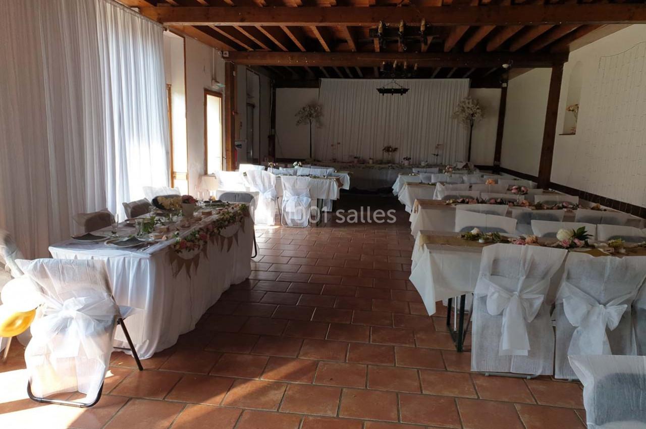 Salle de réception décorée pour un événement, avec tables dressées et chaises couvertes de housses blanches.