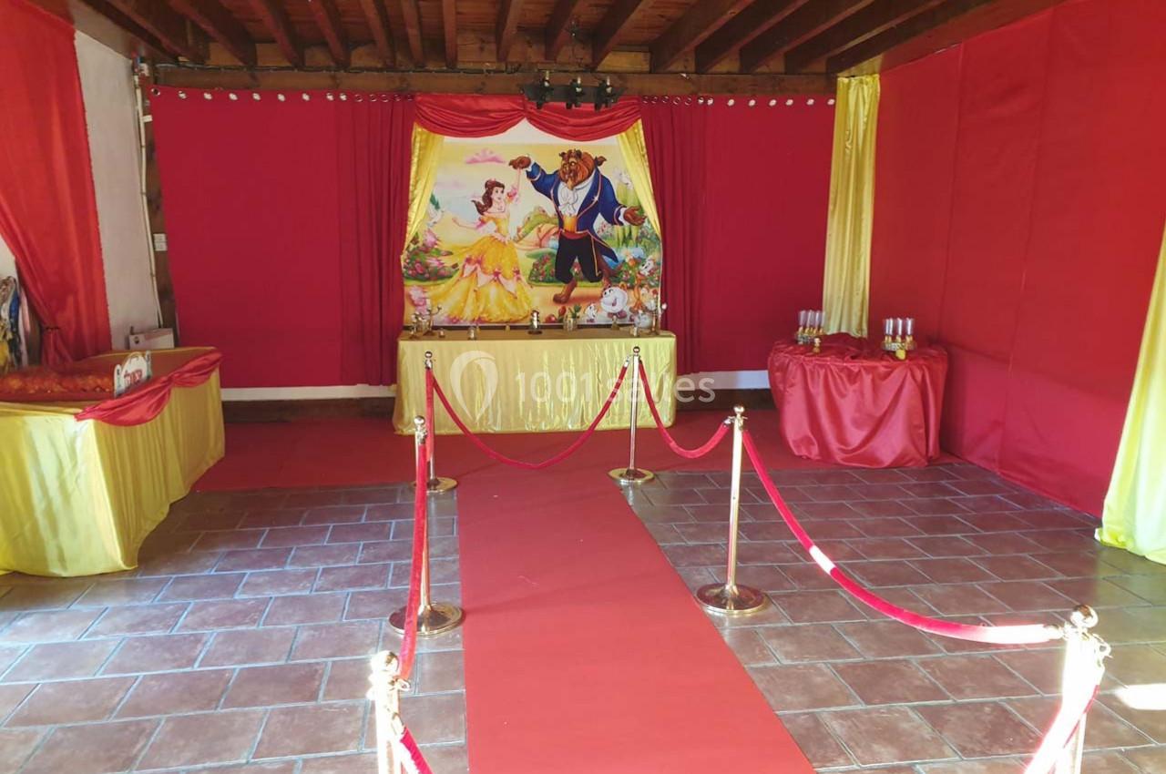 Salle décorée en rouge et jaune avec un tapis rouge, des cordons dorés et une affiche de ’La Belle et la Bête’.
