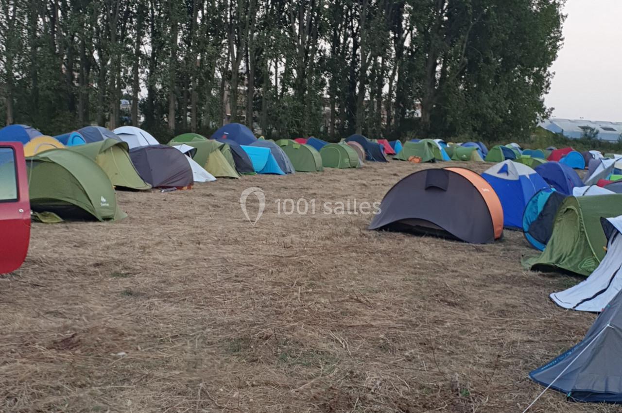 Plusieurs tentes colorées installées sur un terrain herbeux entouré d'arbres.