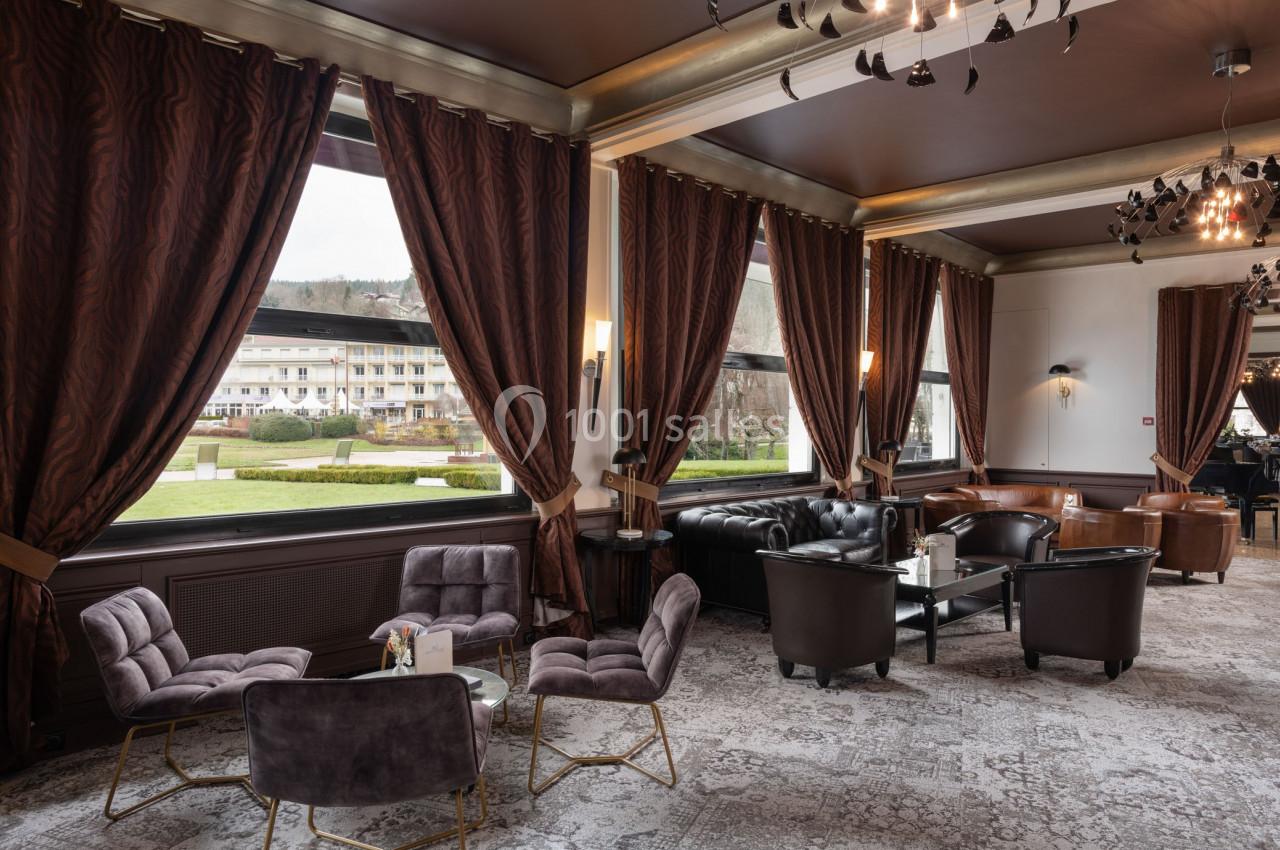 Salon élégant avec fauteuils en velours, canapé en cuir, grandes fenêtres donnant sur un jardin et rideaux sombres.