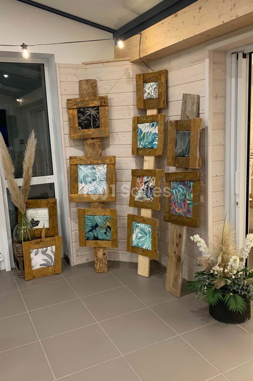 Cadres en bois contenant des illustrations végétales, disposés contre un mur en bois clair dans un espace intérieur.