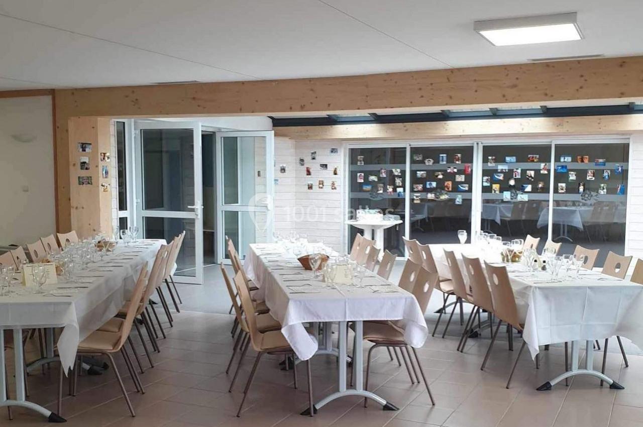Salle lumineuse aménagée pour un repas, avec des tables dressées et des chaises, décorée de photos au mur.