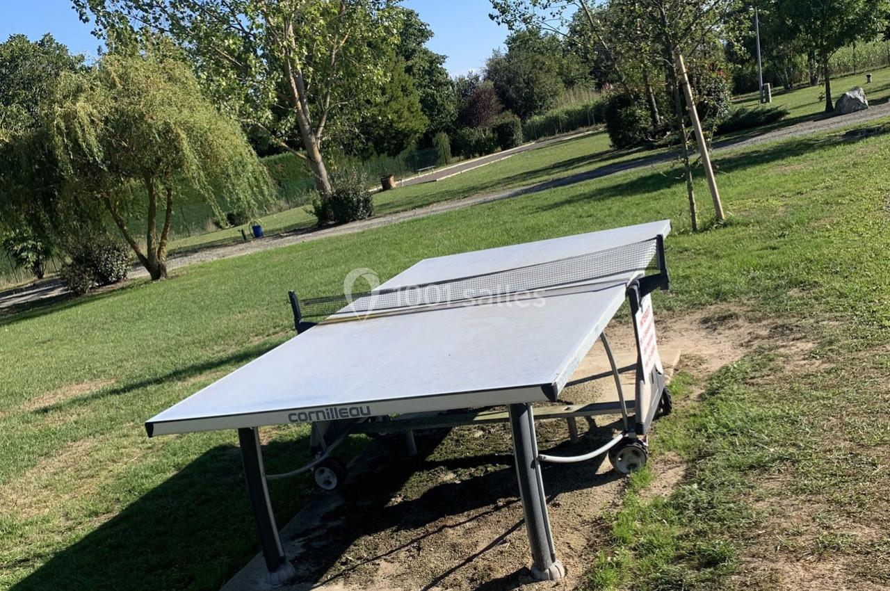 Table de ping-pong extérieure en béton située dans un parc verdoyant avec arbres et pelouse.