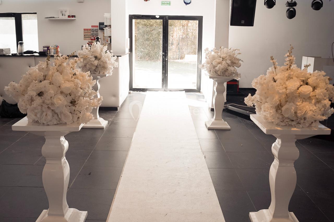 Location salle Roquevaire (Bouches-du-Rhône) - Nao Athéna #7 Allée centrale décorée de colonnes blanches ornées de bouquets de fleurs blanches dans une salle lumineuse.