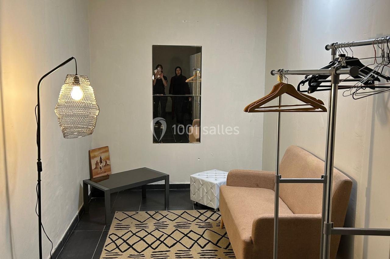 Location salle Roquevaire (Bouches-du-Rhône) - Nao Athéna #17 Salle minimaliste avec canapé beige, miroir, portants à vêtements, tapis géométrique et lampe suspendue.
