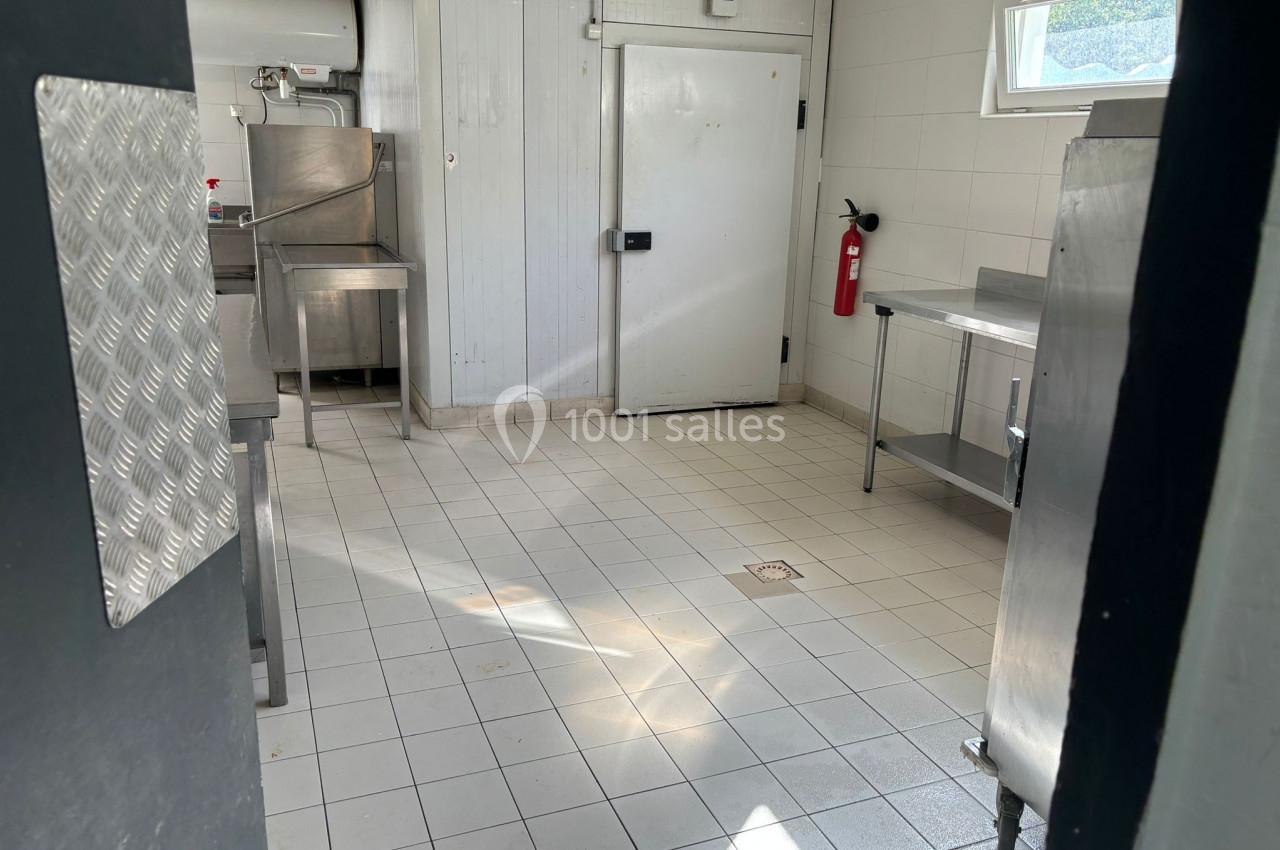 Location salle Roquevaire (Bouches-du-Rhône) - Nao Athéna #20 Cuisine professionnelle vide avec équipements en inox, sol carrelé, porte froide et extincteur fixé au mur.