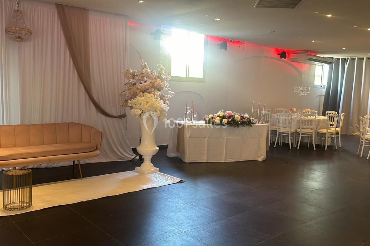 Location salle Roquevaire (Bouches-du-Rhône) - Nao Athéna #5 Salle décorée pour un événement avec canapé beige, rideaux blancs, fleurs et tables dressées.
