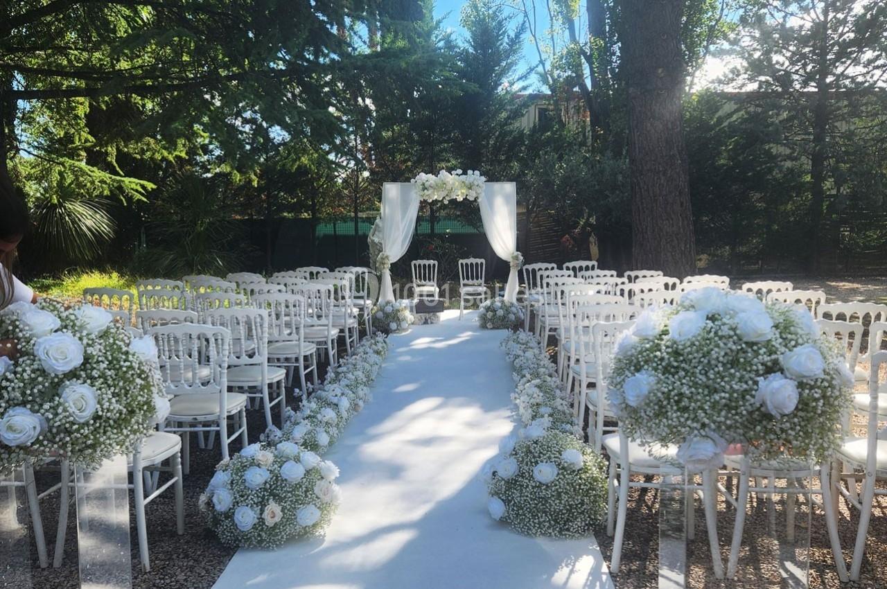 Location salle Roquevaire (Bouches-du-Rhône) - Nao Athéna #12 Allée centrale décorée de fleurs blanches menant à une arche nuptiale dans un cadre extérieur boisé.