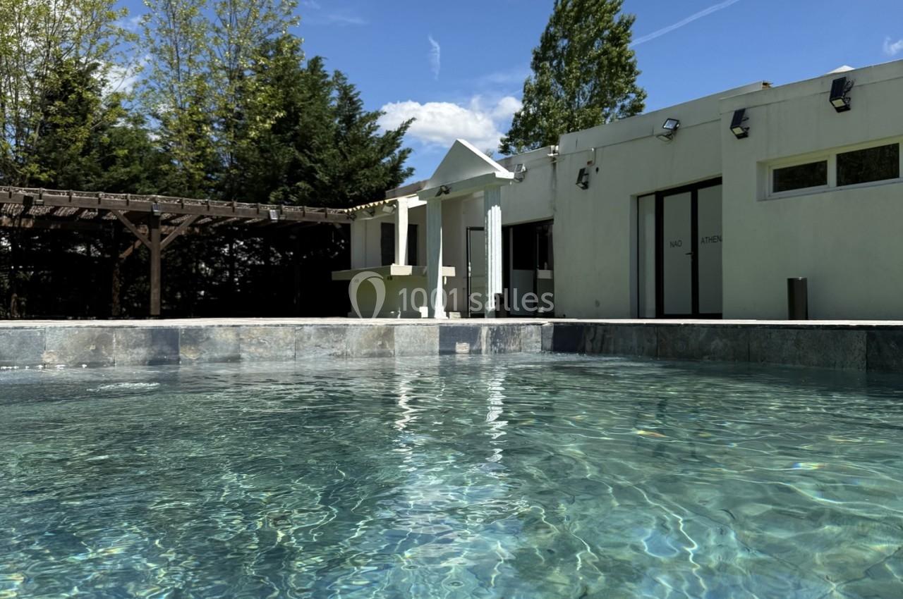 Location salle Roquevaire (Bouches-du-Rhône) - Nao Athéna #9 Piscine extérieure avec eau claire, entourée d'une terrasse, d'arbres et d'un bâtiment moderne sous un ciel dégagé.