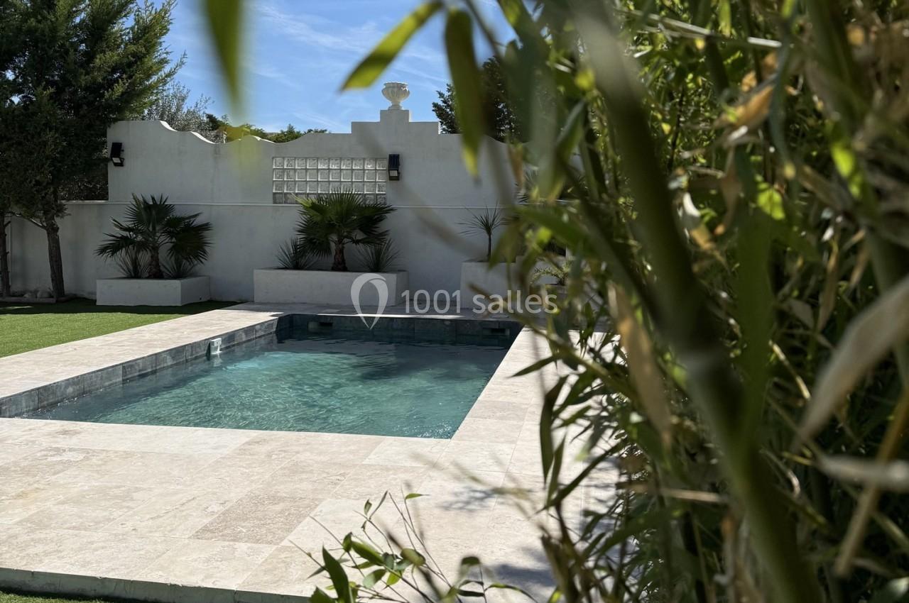 Location salle Roquevaire (Bouches-du-Rhône) - Nao Athéna #11 Piscine rectangulaire entourée de végétation et de dalles claires, avec un mur blanc en arrière-plan.