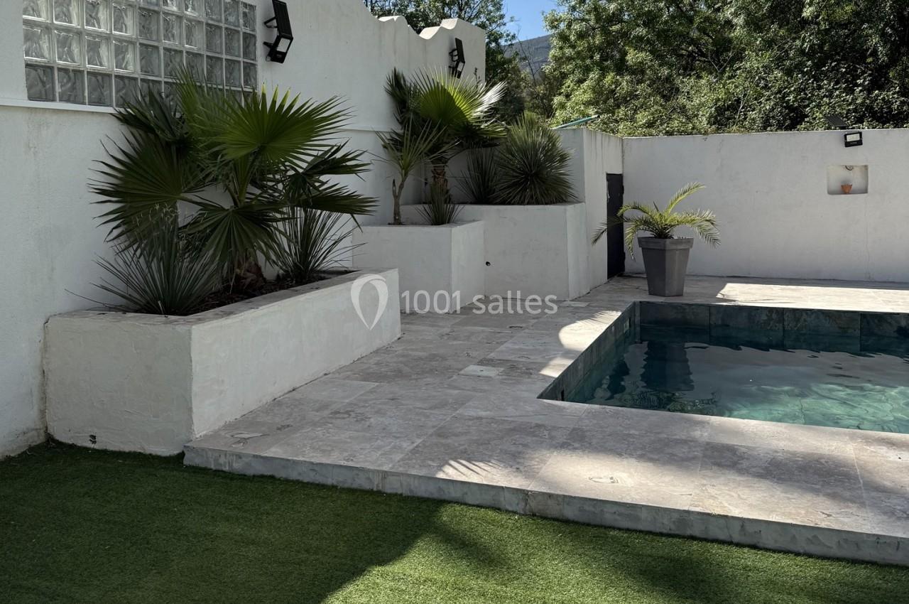 Location salle Roquevaire (Bouches-du-Rhône) - Nao Athéna #21 Piscine entourée de dalles en pierre, avec des plantes en pots et un mur blanc en arrière-plan.