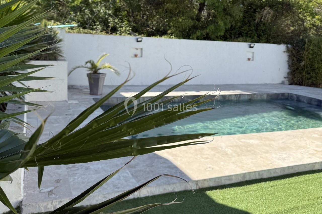 Location salle Roquevaire (Bouches-du-Rhône) - Nao Athéna #30 Vue d'une piscine entourée de dalles claires, avec un palmier au premier plan et un mur blanc en arrière-plan.