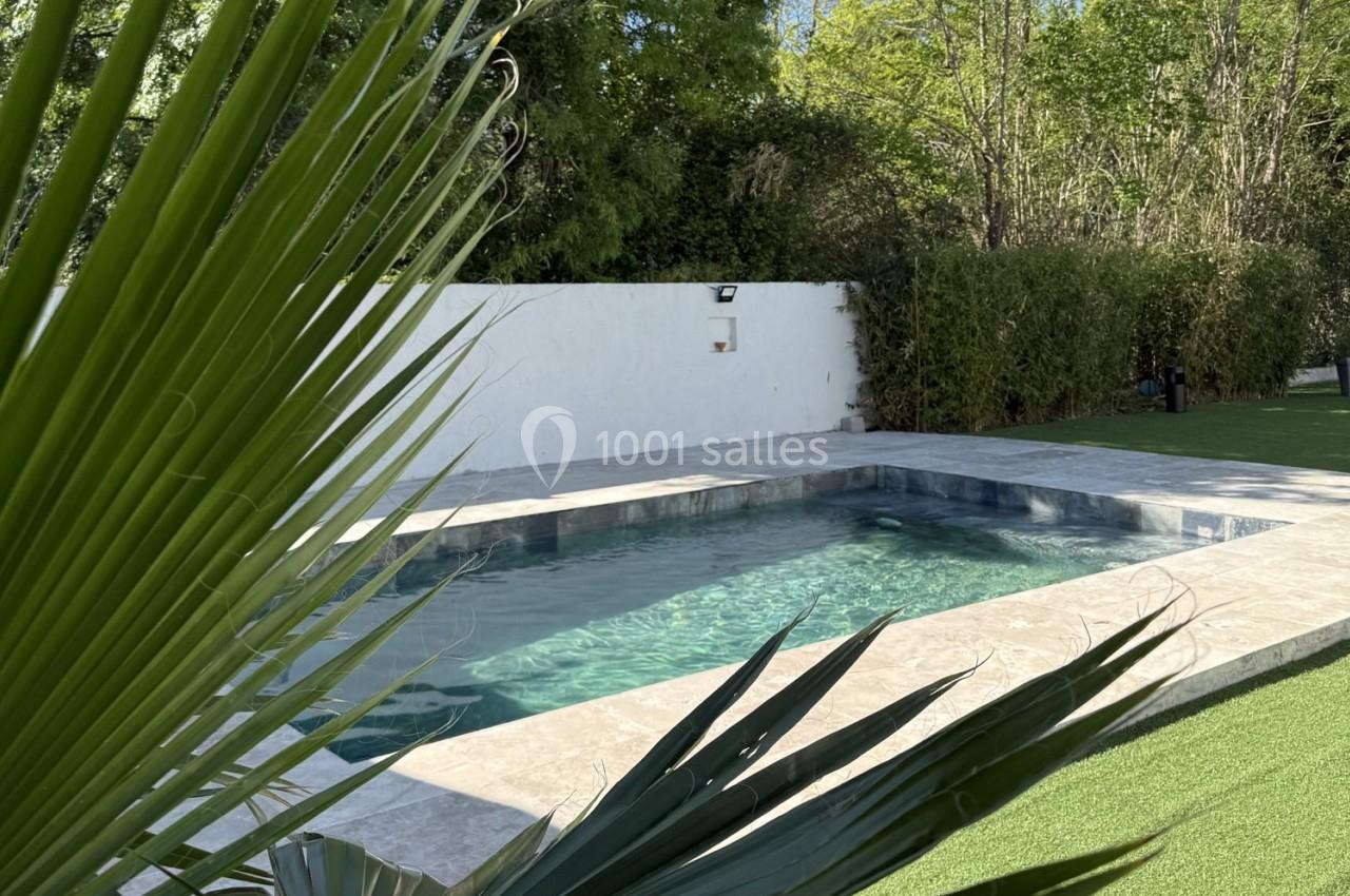 Location salle Roquevaire (Bouches-du-Rhône) - Nao Athéna #31 Piscine extérieure entourée de dalles en pierre, avec pelouse artificielle, haies et arbres en arrière-plan.