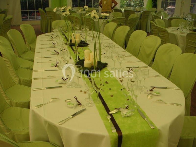 Table décorée avec une nappe blanche, chemin de table vert, bougies, fleurs blanches et vaisselle élégante.