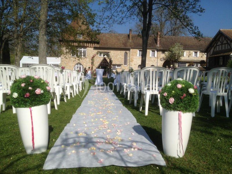 Allée décorée de pétales et de fleurs menant à une cérémonie en plein air devant un bâtiment en pierre.