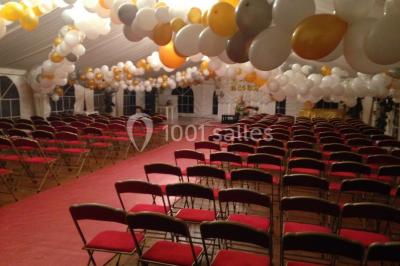 Miniature Location salle Rosay (Yvelines) - Manoir des Foulons #22 Salle décorée avec des ballons blancs et dorés, rangées de chaises rouges alignées sur un tapis rouge.