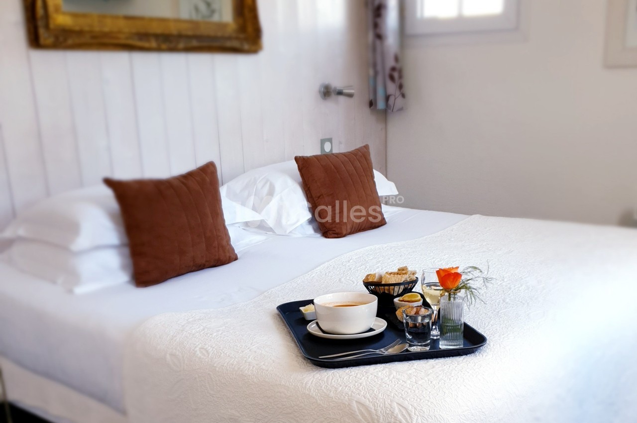 Plateau petit-déjeuner avec tasse, jus et viennoiseries posé sur un lit blanc dans une chambre lumineuse.