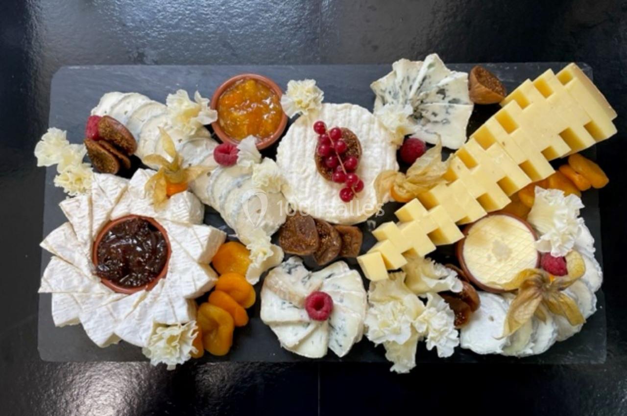 Plateau de fromages variés avec fruits secs, confitures et décoration sur une ardoise noire.