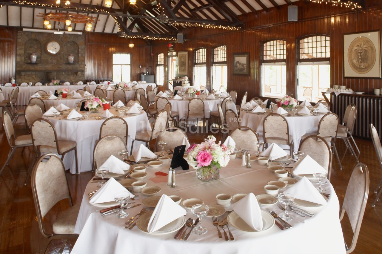 Salle de réception avec tables rondes dressées, nappes blanches, serviettes pliées et centres de table fleuris.