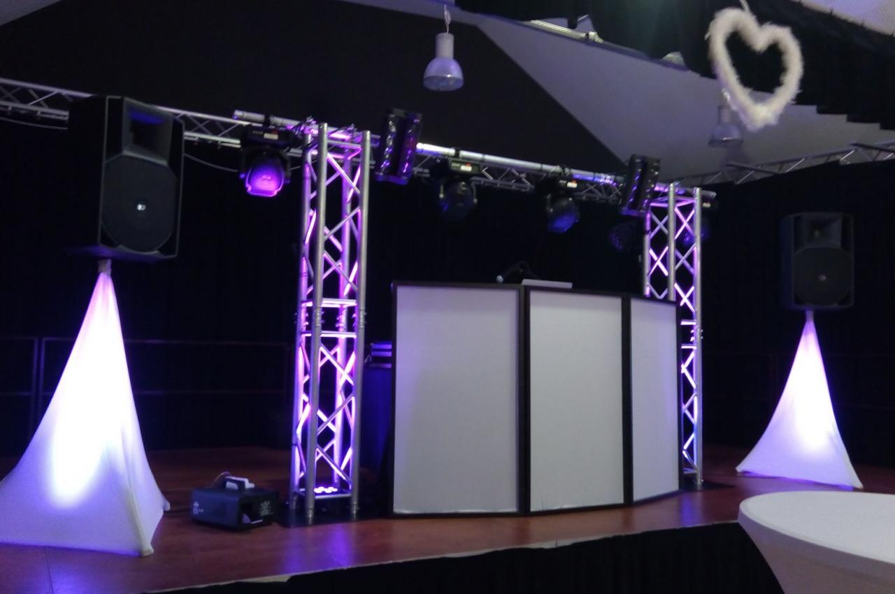 Installation de matériel de sonorisation et éclairage avec une cabine DJ sur une scène, décorée de lumières violettes.
