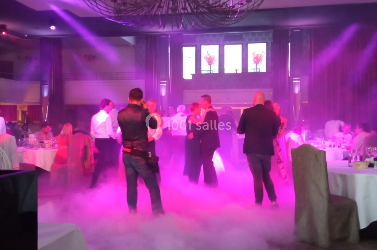 Personnes dansant dans une salle de réception éclairée par des lumières colorées et entourée de fumée au sol.