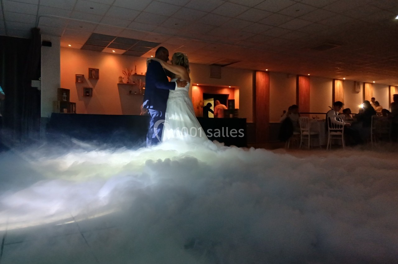 Un couple danse au milieu d'une piste enveloppée de fumée, dans une salle faiblement éclairée.