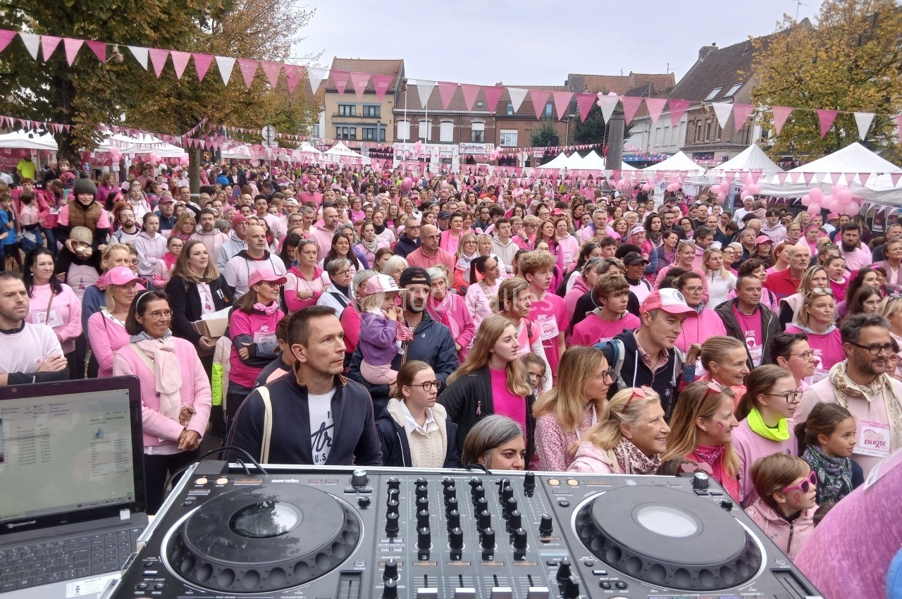 Foule vêtue de rose rassemblée sur une place pour un événement, vue depuis une table de mixage au premier plan.