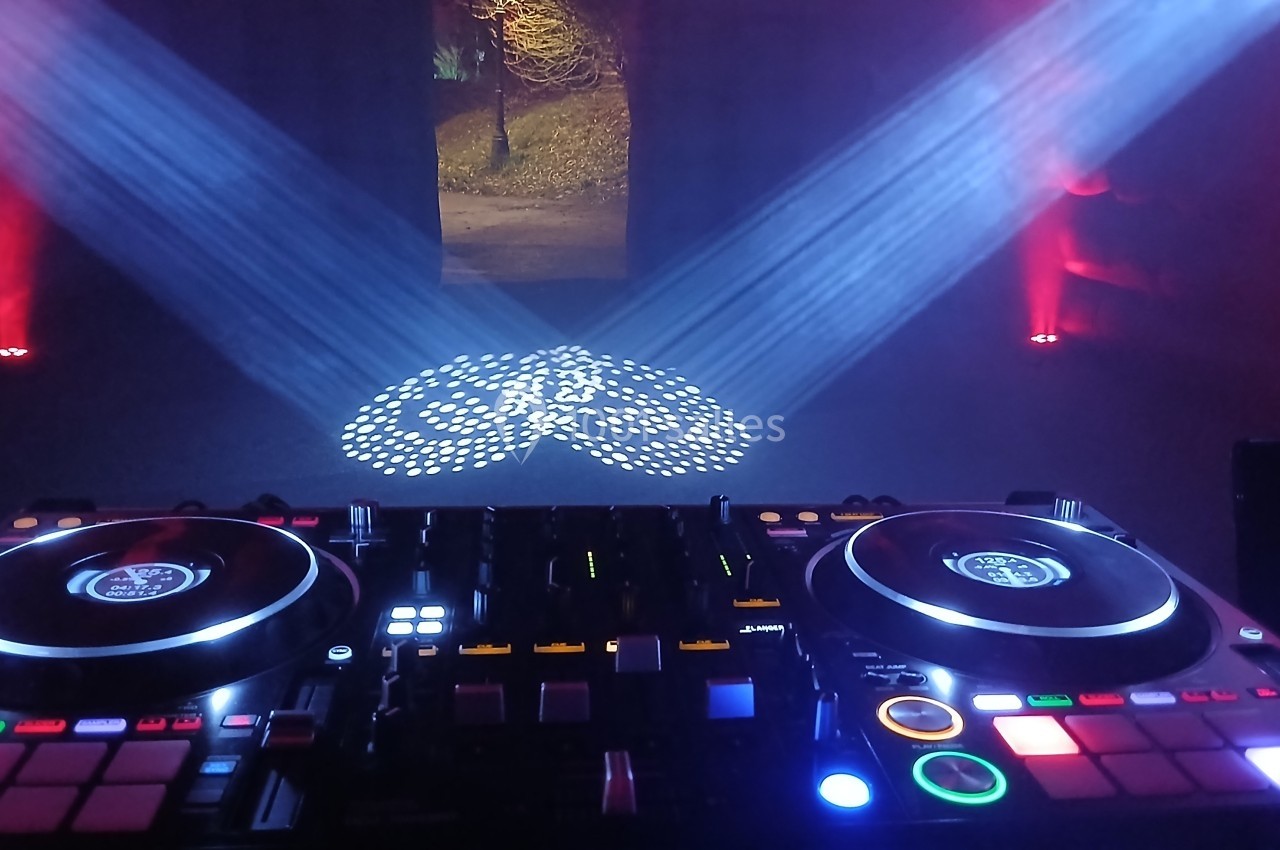 Console de mixage DJ éclairée avec des projecteurs colorés et motifs lumineux au sol dans une ambiance sombre.