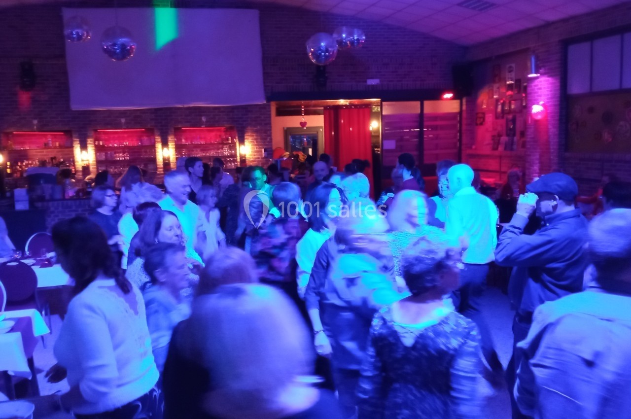 Groupe de personnes dans une salle éclairée par des lumières colorées, certaines dansent, d'autres discutent.