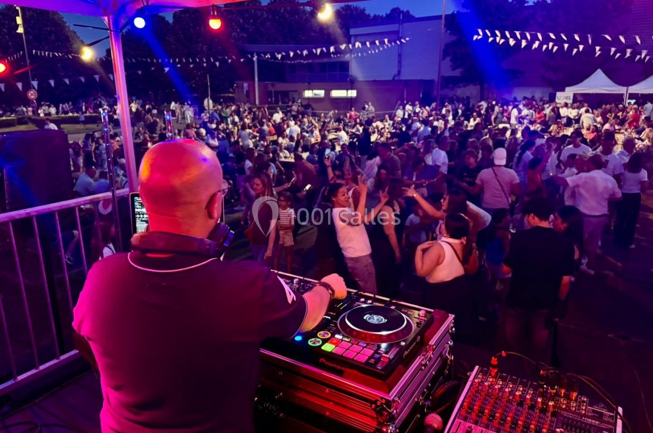 Un DJ anime une soirée en plein air avec une foule dansante sous des guirlandes lumineuses.