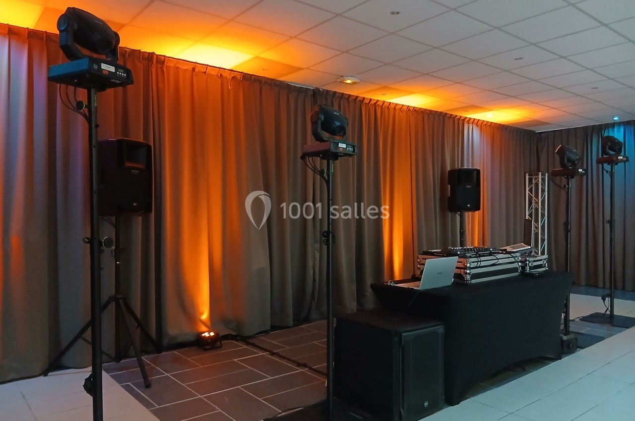Équipement de sonorisation et éclairage avec rideaux orange en arrière-plan dans une salle événementielle.
