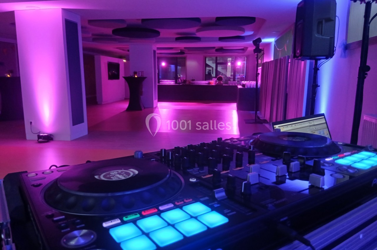 Console de DJ en premier plan dans une salle éclairée par des lumières violettes, avec un bar en arrière-plan.