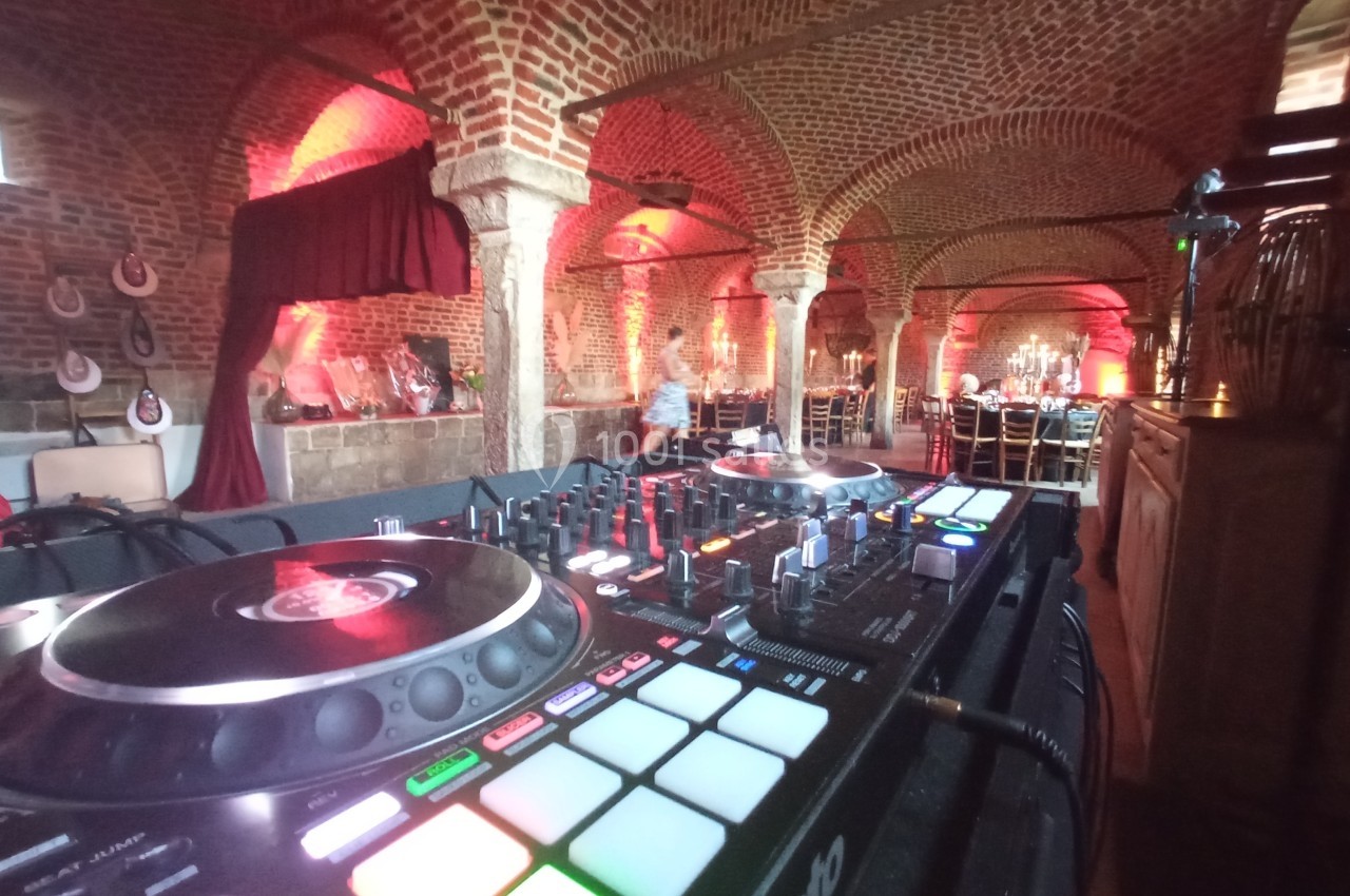 Table de mixage dans une salle voûtée en briques rouges, éclairée par des lumières tamisées et décorée pour un événement.