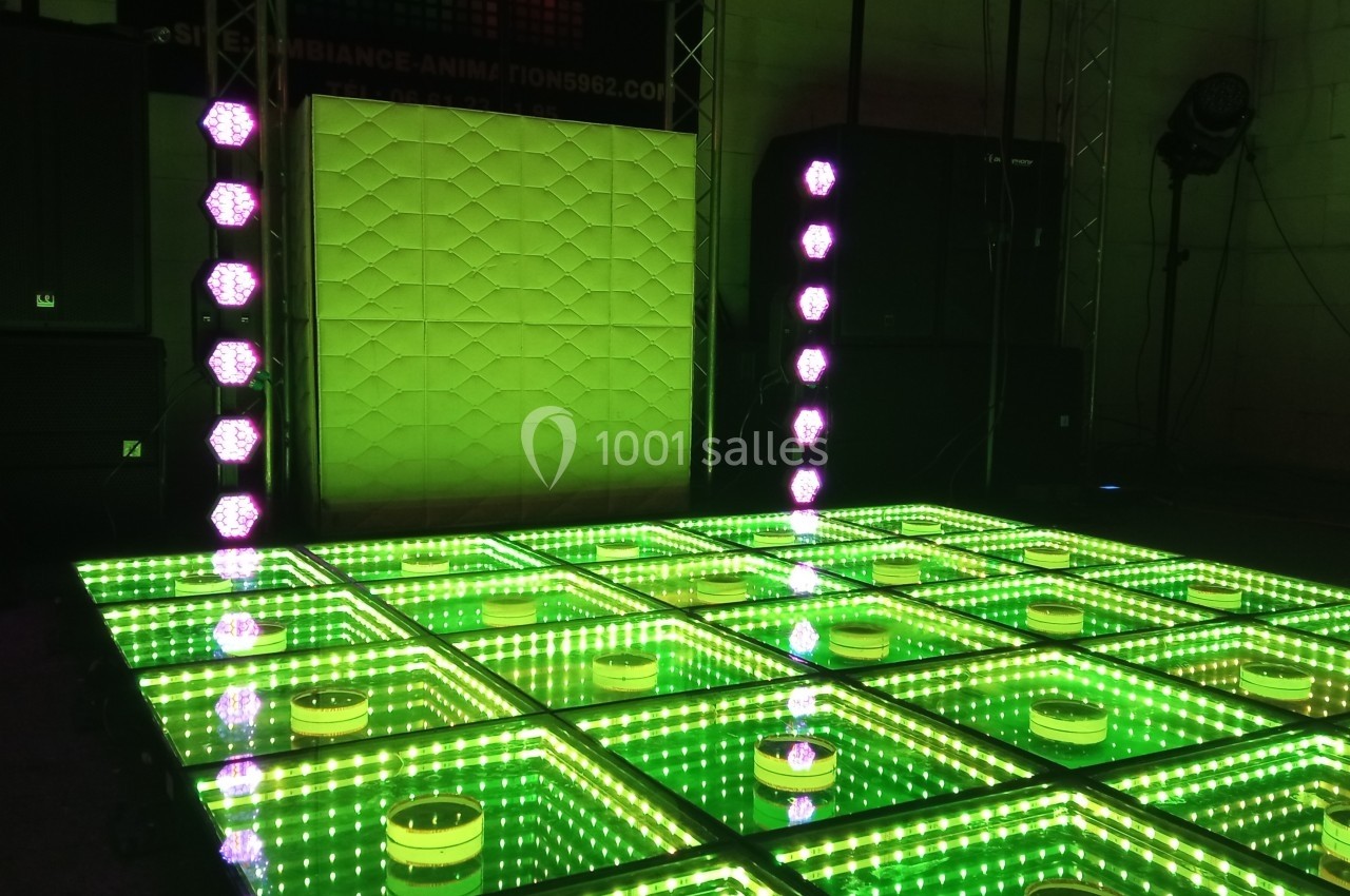 Piste de danse lumineuse avec des carreaux verts réfléchissants et des colonnes de lumières LED violettes.
