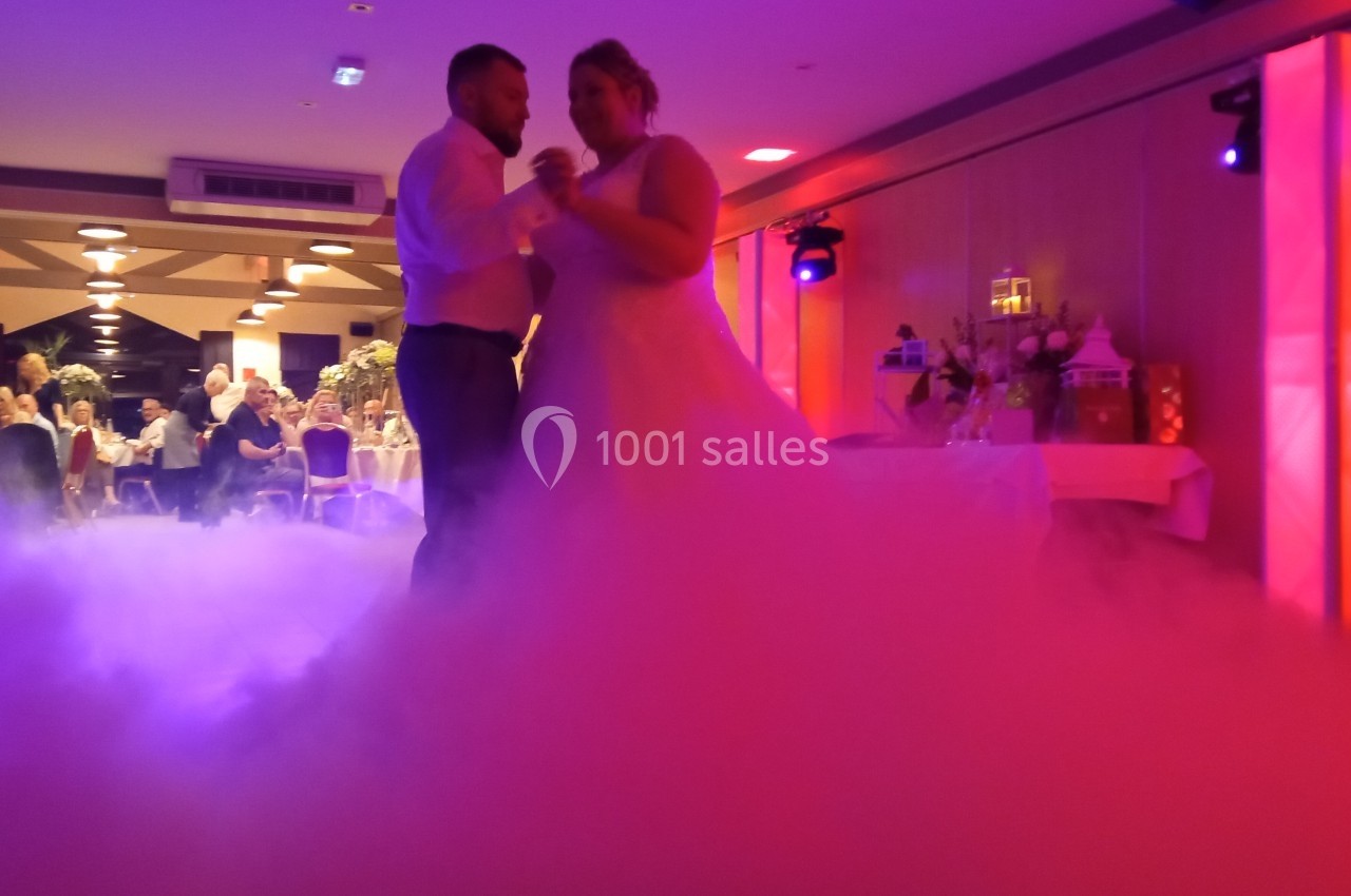 Un couple danse dans une salle de réception éclairée, entouré d'un effet de fumée au sol.