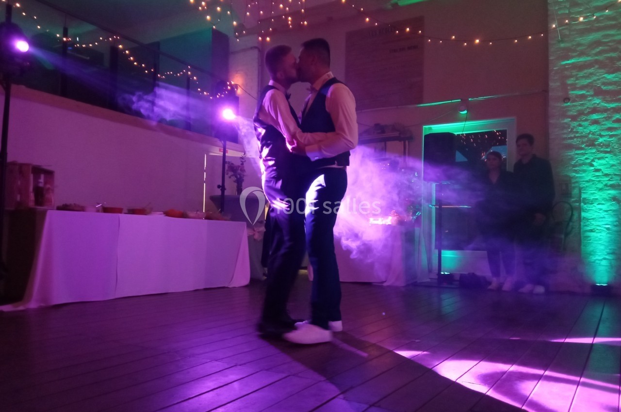 Deux hommes dansent ensemble sur une piste éclairée par des lumières colorées dans une ambiance festive.