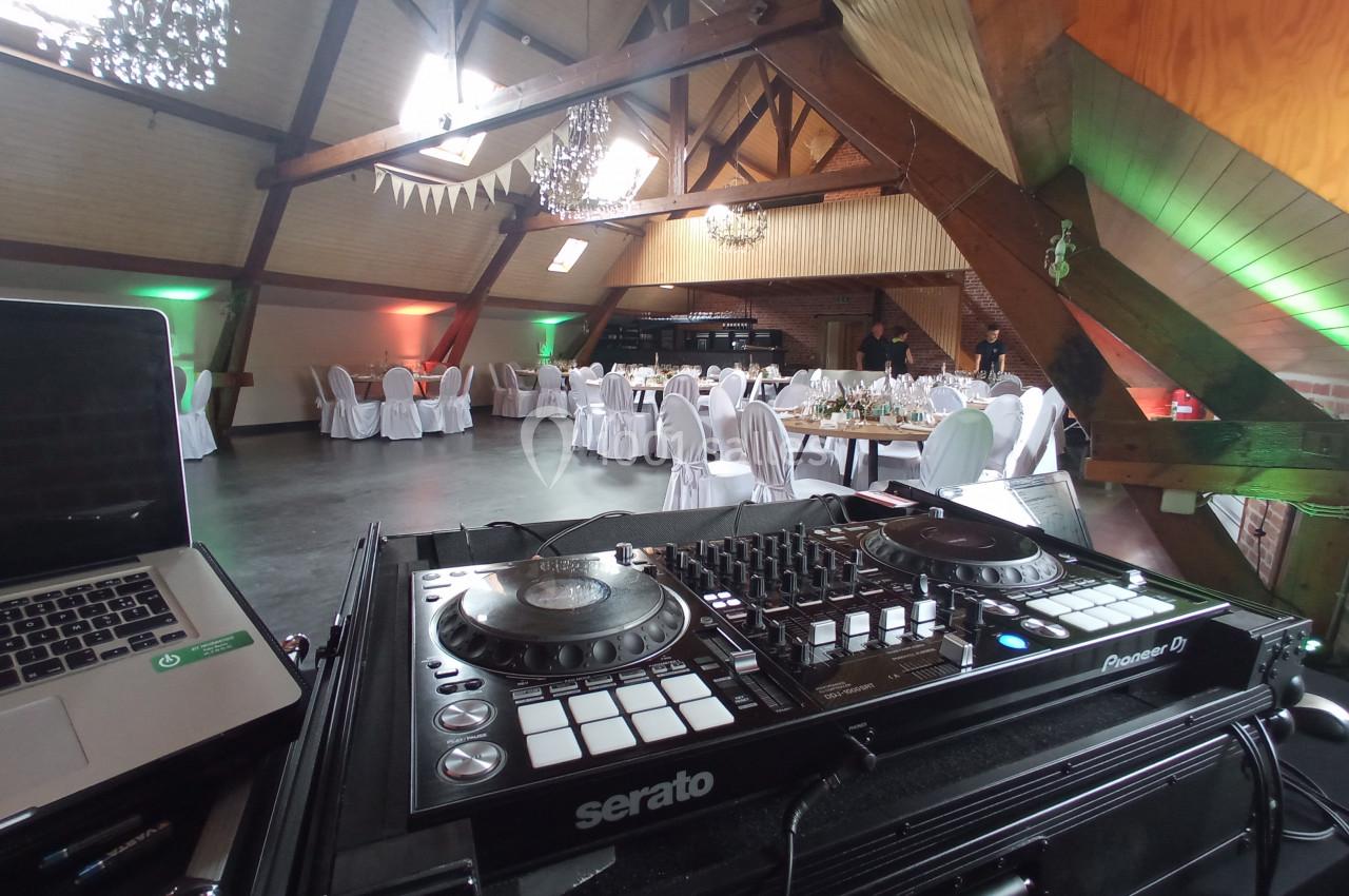 Salle de réception décorée avec des tables dressées, vue depuis une console de DJ équipée de platines.