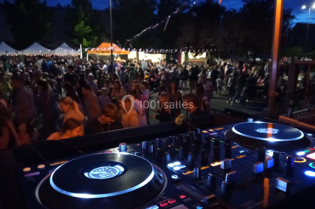 Vue d'une table de mixage en premier plan avec une foule rassemblée lors d'un événement en plein air, de nuit.