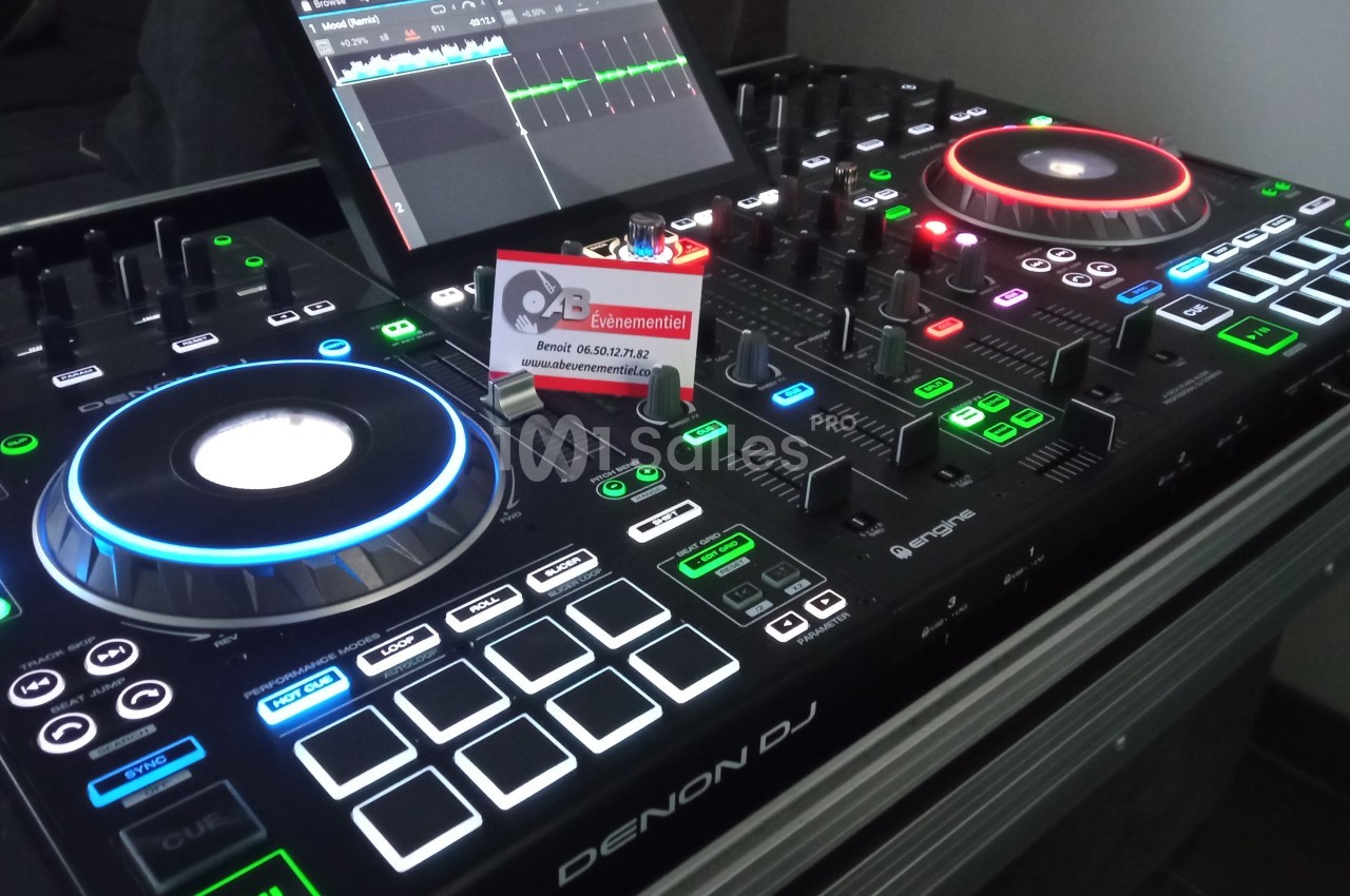 Table de mixage Denon DJ avec éclairages colorés, écran tactile et carte de visite posée au centre.