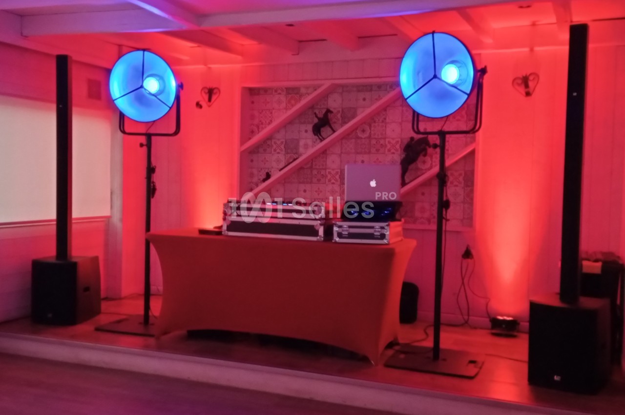 Équipement de DJ avec table de mixage, ordinateur portable et éclairage bleu dans une salle à la décoration chaleureuse.