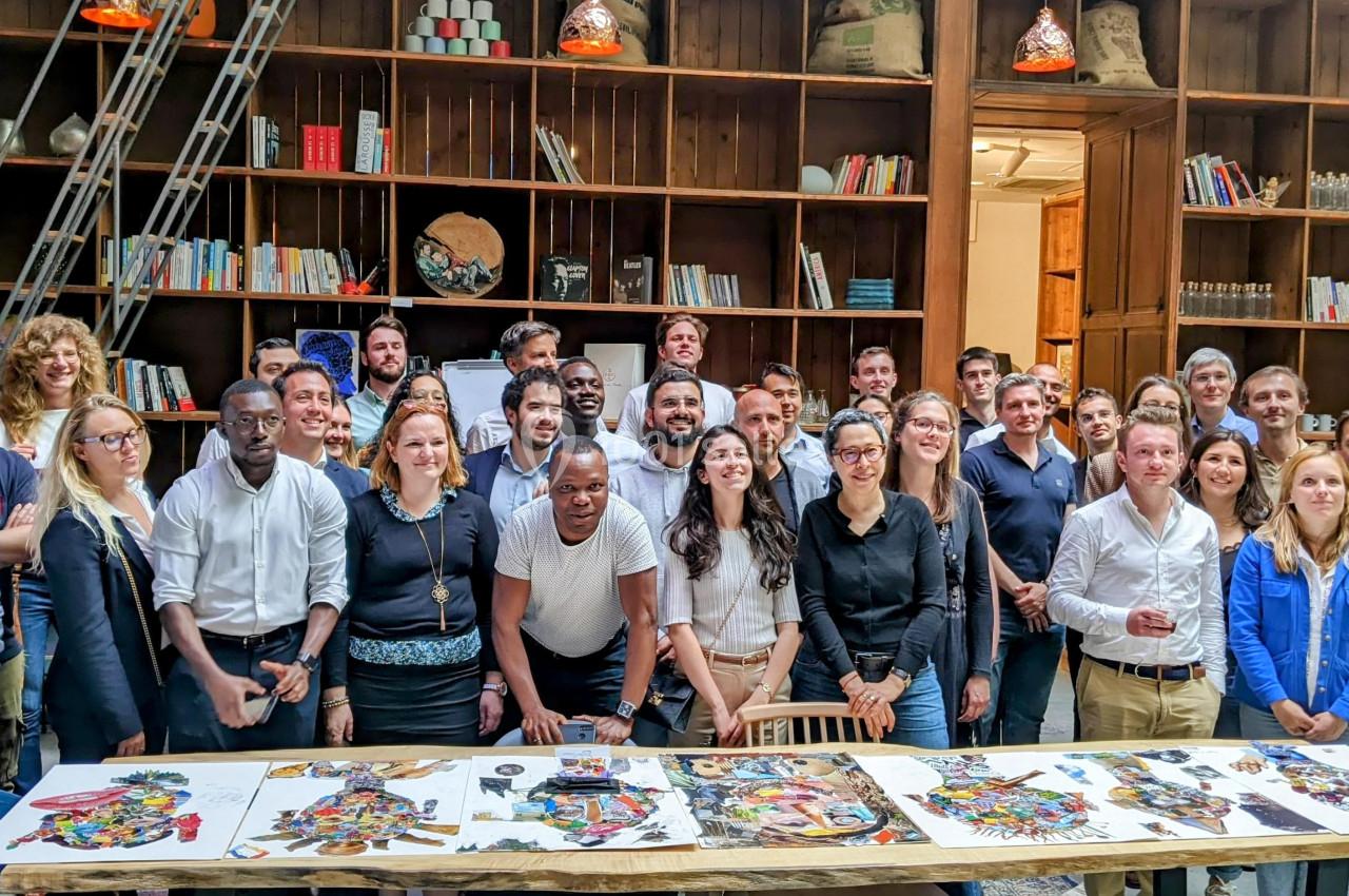 Un groupe de personnes pose devant une table avec des œuvres colorées, dans une pièce avec des étagères remplies de livres.