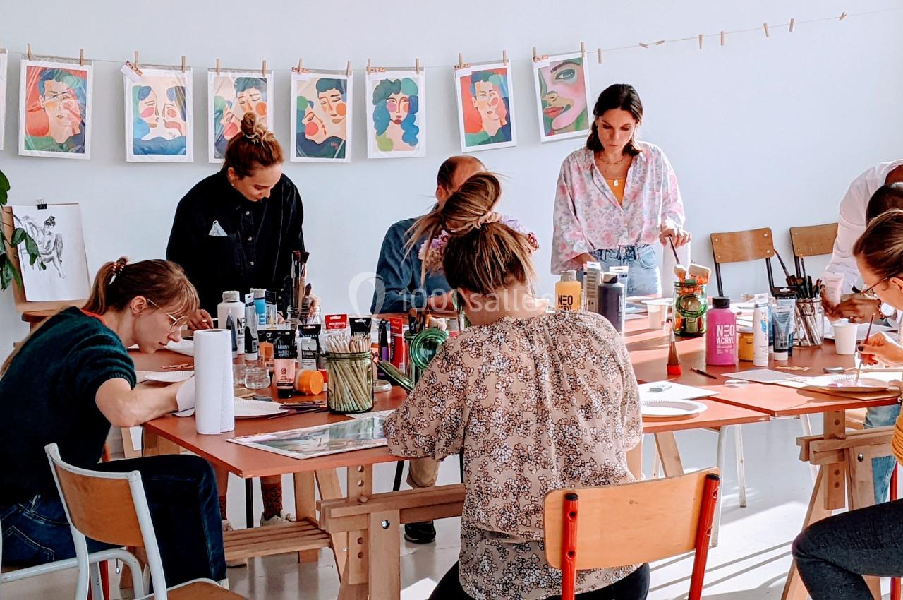Des personnes participent à un atelier artistique, dessinant et peignant autour d'une grande table dans une salle lumineuse.
