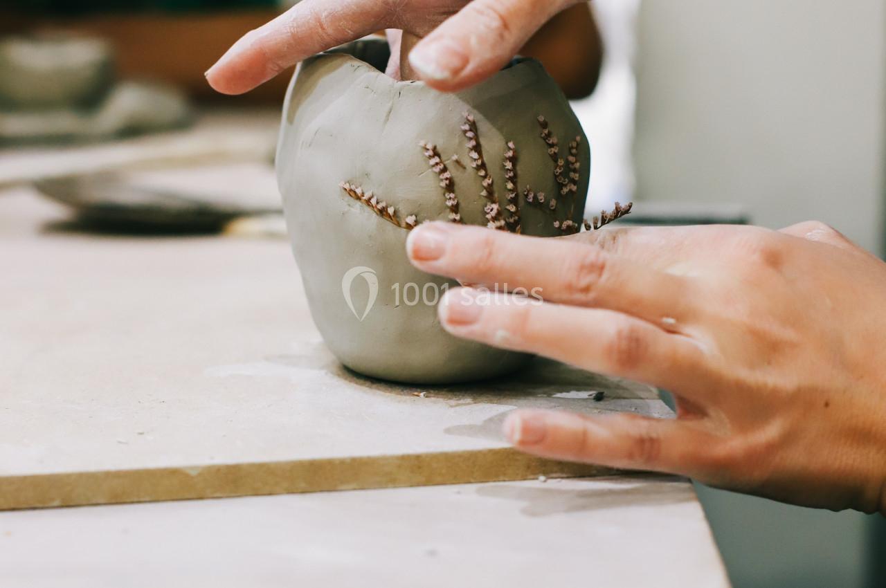 Deux mains façonnent une pièce en argile ornée de motifs, posée sur une table de travail.
